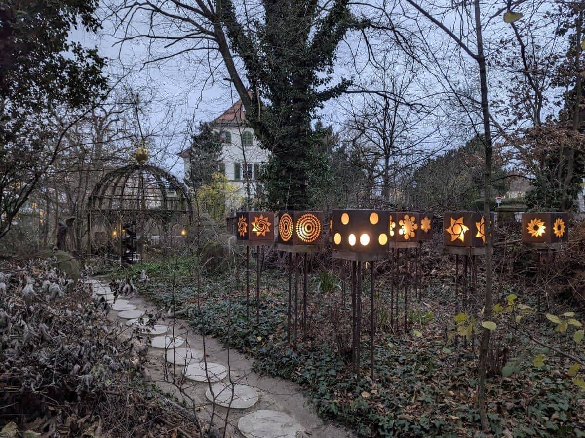 stimmungsvolle Szene im Vortex Garten mit dekorativen Laternen und einem einladenden Pavilon, harmonisch eingebettet in die Natur